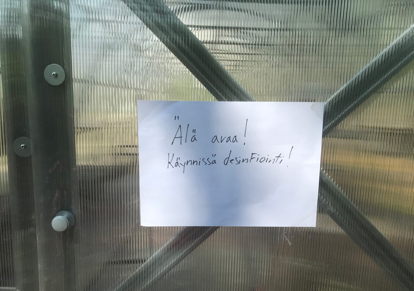 Käsinkirjoitettu lappu kasvihuoneen ovessa. Lapussa lukee. Älä avaa. Käynnissä desinfiointi.